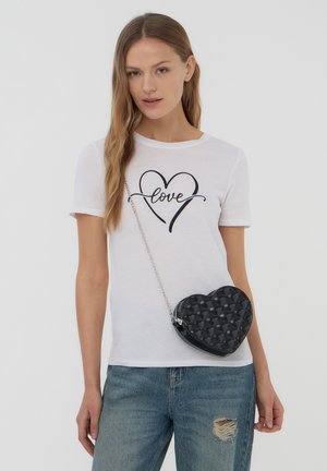 T-shirt bianca con grafica a cuore nero e testo "love", abbinata a una borsa a forma di cuore nera con superficie testurizzata e tracolla in metallo argentato.