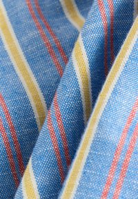 Katoenen stof in het blauw met verticale strepen in rood, geel en wit. Zachte textuur met een gemêleerd patroon, met variërende streepbreedtes.
