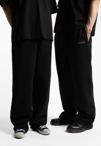 Schwarz oversized Hose aus weichem Stoff, mit lässigem Schnitt und dezentem Logodetail. Kombiniert mit lässigen Sneakern und Clogs.