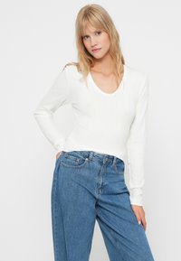 Hvid langærmet ribbet top med scoop halsudskæring, parret med højtaljede blå denimjeans med løst fit og fem-lomme design.