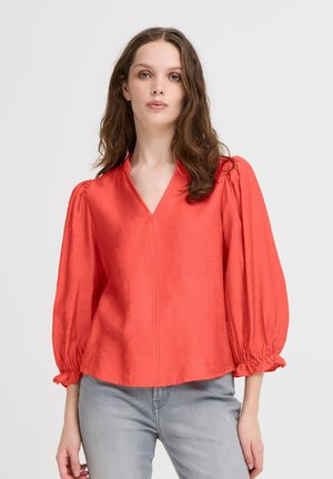Blouse rouge à col en V avec des manches bouffantes et des poignets froncés. Fabriquée en tissu lisse, elle présente une coupe droite et une texture subtile.