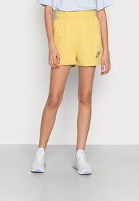 Shorts en coton jaune avec une taille élastique, dotés de coutures latérales et d'un petit détail logo. Assortis à des baskets blanches en mesh.