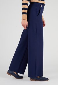 Marineblauwe wijde broek met een gladde textuur, hoge tailleband en zijzakken. Gecombineerd met blauwe suède instappers, wat een klassieke look laat zien.