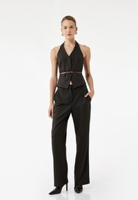 Completo su misura nero a righe con top senza maniche e cintura, abbinato a pantaloni a gamba larga. Presenta una scollatura a V profonda e una texture di tessuto liscia.