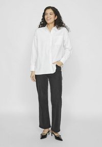 Camisa blanca de botones con mangas largas, un solo bolsillo en el pecho, combinada con pantalones negros de pierna recta y tacones negros de punta.