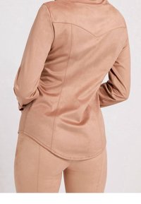 Lysrosa faux suede skjorte med lange ærmer, buet kant og en tætsiddende silhuet. Har dartdetaljer på ryggen.