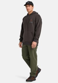 Gray hooded sweatshirt with pouch pocket, featuring an orange and teal logo. Paired with olive green pants and brown hiking shoes.