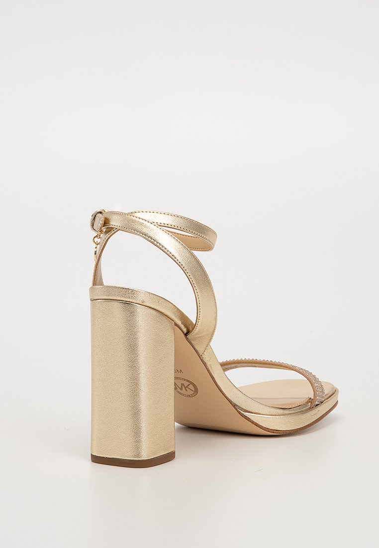Sandale à talon haut dorée avec un large talon bloc, bout ouvert, bride de cheville réglable et accents en strass sur la bride. Fini métallique lisse.