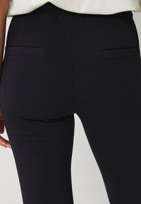 Sorte stretch-bukser med en glat stofstruktur, slim fit og doble baglommer med et enkelt, rent design.