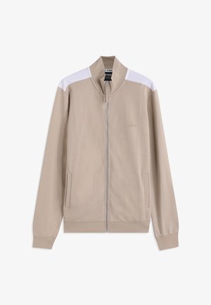 Giacca beige con zip, collo alto, dettagli bianchi sulle spalle e tasche laterali. Realizzata in tessuto liscio con design aderente.