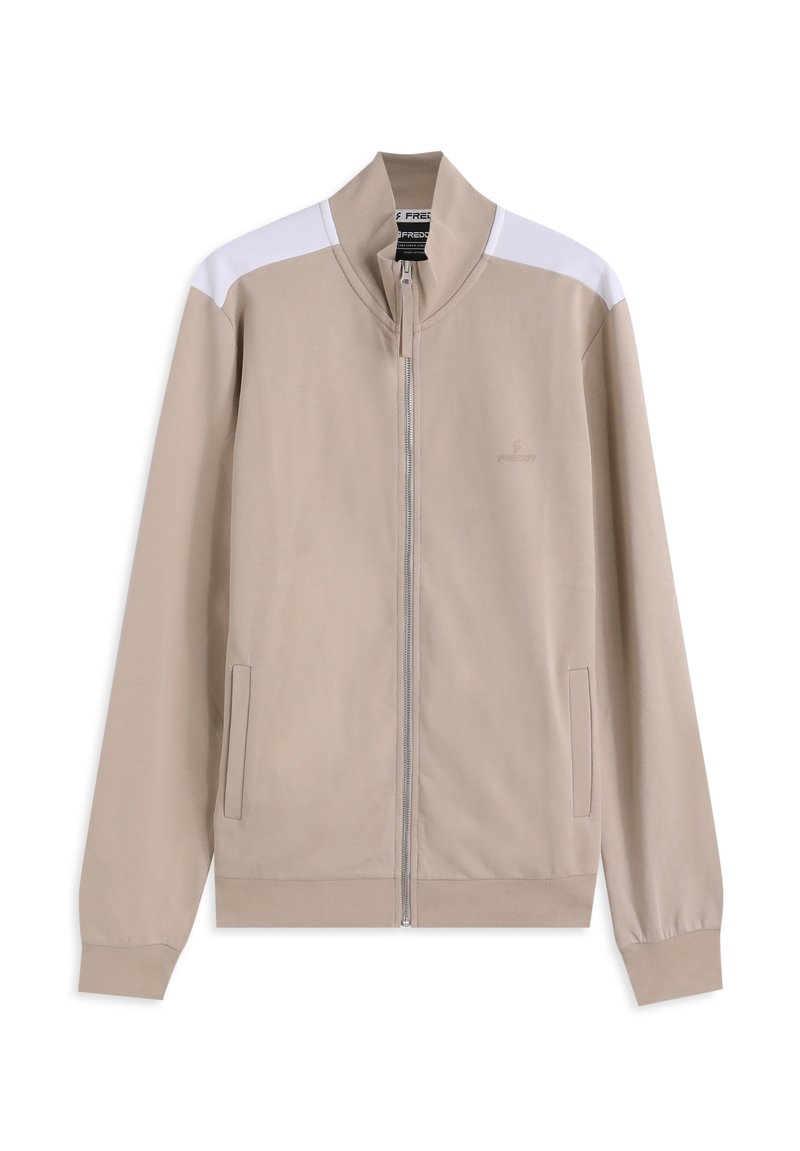 Chaqueta beige con cremallera, con cuello alto, acentos blancos en los hombros y bolsillos laterales. Hecha de tela suave con un diseño ajustado.
