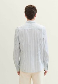 Camisa ligera de manga larga a rayas blancas y azules. Presenta un cuello clásico, puños abotonados y un dobladillo curvado. Textura de tela suave.