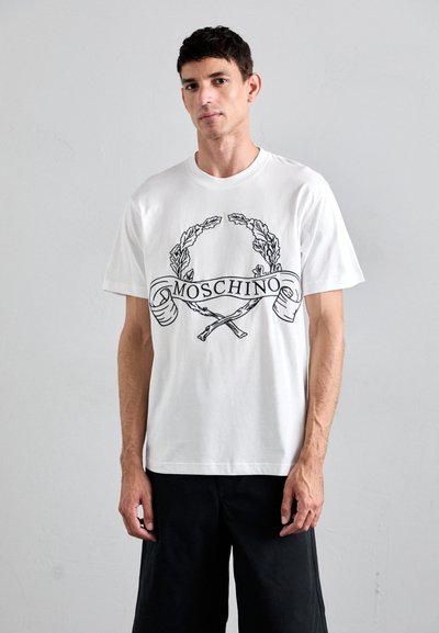 Biała bawełniana koszulka z czarnym wzorem graficznym przedstawiającym liście laurowe oraz wstęgą z napisem "Moschino" i dwoma skrzyżowanymi młotkami. Krótkie rękawy.