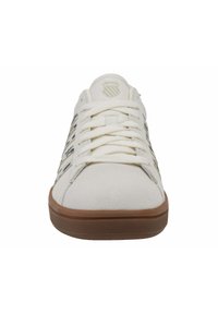 Baskets en suede blanches avec une semelle en caoutchouc naturel, dotées de lacets plats, d'un logo sur la languette et de subtils accents de design sur les côtés.