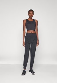 Čierny crop top s rebrovanou textúrou, skombinovaný s čiernymi zúženými nohavicami s elastickým pásom a manžetami na členkoch a čiernymi športovými topánkami s ružovými akcentmi.