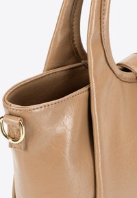 Beige Ledertasche mit glatter Textur, die über zwei stabile Griffe und einen Akzent in goldfarbener Hardware verfügt. Der offene oberen Bereich ermöglicht den Zugang zum Innenraum.