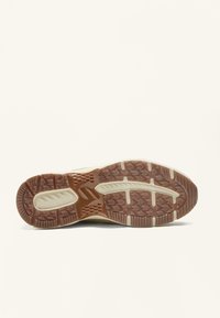 Grå sneakersål med en tekstureret brun gummiydersål, som har riller og mønstre for greb og stabilitet.