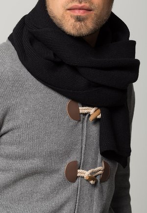 Schwarzer Strickschal, der um den Hals drapiert ist, kombiniert mit einem grauen Pullover mit braunen Toggle-Knöpfen und Seilakzenten.