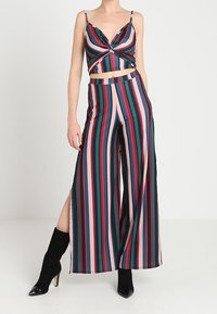 Pruhovaný dvoudílný set, který zahrnuje crop top s twist předním dílem a volné kalhoty. Barvy zahrnují zelenou, růžovou a černou s rozparky. Hladká látka.