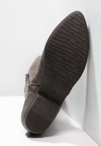 Stivaletto in pelle scamosciata marrone, caratterizzato da una suola in gomma testurizzata con un motivo a zigzag, chiusura con zip sul lato e marchio sulla suola.