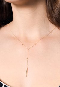 Złota naszyjnik z wiszącym wisiorkiem o smukłym kształcie, z małymi sferycznymi akcentami i gładkim, błyszczącym wykończeniem.