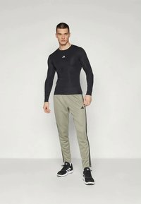 Schwarz langärmliges Sportoberteil mit taillierter Passform, graue tapered Hose mit seitlichen Streifen und schwarze Sportschuhe mit weißen Akzenten.
