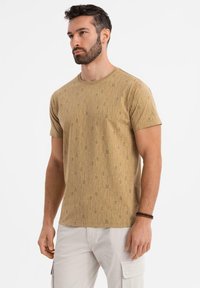 Kortærmet T-shirt med rund hals i let beige stof, der har vertikale tekstmønstre i mørkere beige nuancer. Almindelig pasform.