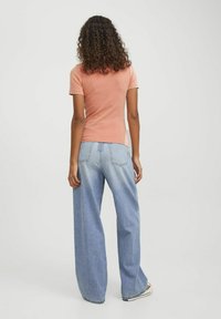 T-shirt aderente color pesca chiaro a costine abbinato a jeans in denim azzurro oversize. I jeans presentano un design classico a cinque tasche.