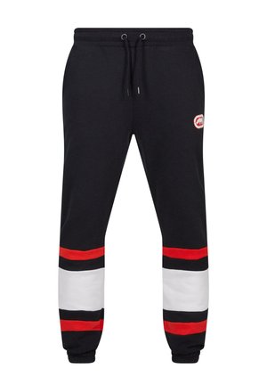Svart joggebukse med røde og hvite horisontale striper ved anklene, snor i livet, og logo-patch på låret. Blandingsmateriale av bomull.