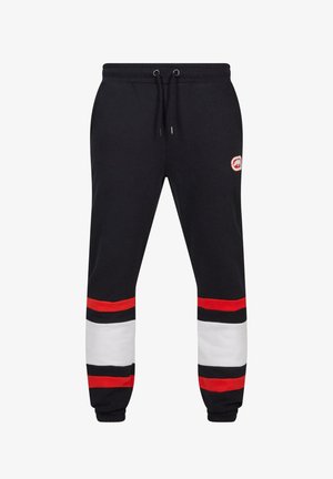 Must have spordipüksid, millel on punased ja valged horisontaalsed triibud pahkluude juures, nööriga vöökoht ja logo tükike reiele. Puuvilla segu materjal.