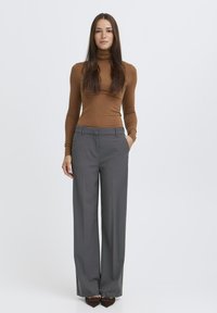 Hnedý tesne priliehajúci rolák skombinovaný s vysokými šedými nohavicami s širokými nohavicami. Nohavice majú predné vrecká a hladkú textúru. Hnedé topánky dotvárajú celkový vzhľad.