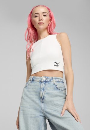 Witte geribde croptop met een asymmetrisch ontwerp en een zwart Puma-logo, gecombineerd met lichtblauwe high-waisted spijkerbroek.