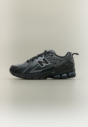 Schwarzer und grauer New Balance Laufschuh mit der Aufschrift "1906", weißen Akzenten und durchsichtiger, luftgepolsterter Sohle auf neutralem Hintergrund.