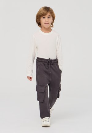 Bambino che indossa una maglietta bianca a maniche lunghe e pantaloni cargo grigi scuri con tasche laterali. I pantaloni hanno una vita elasticizzata e un fit rilassato.