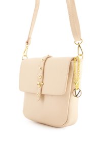 Beige læder crossover taske med klap, guldfarvet hardware, nitter og en charme med et hjerte og logo. Glat tekstur, rektangulær form.