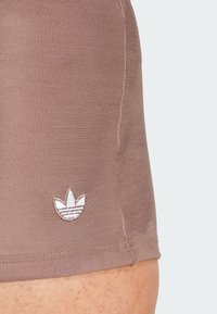 Hnědé sportovní šortky s hladkou texturou, na lemu mají malé bílé vyšívané logo. Jednoduchý design bez vzorů.