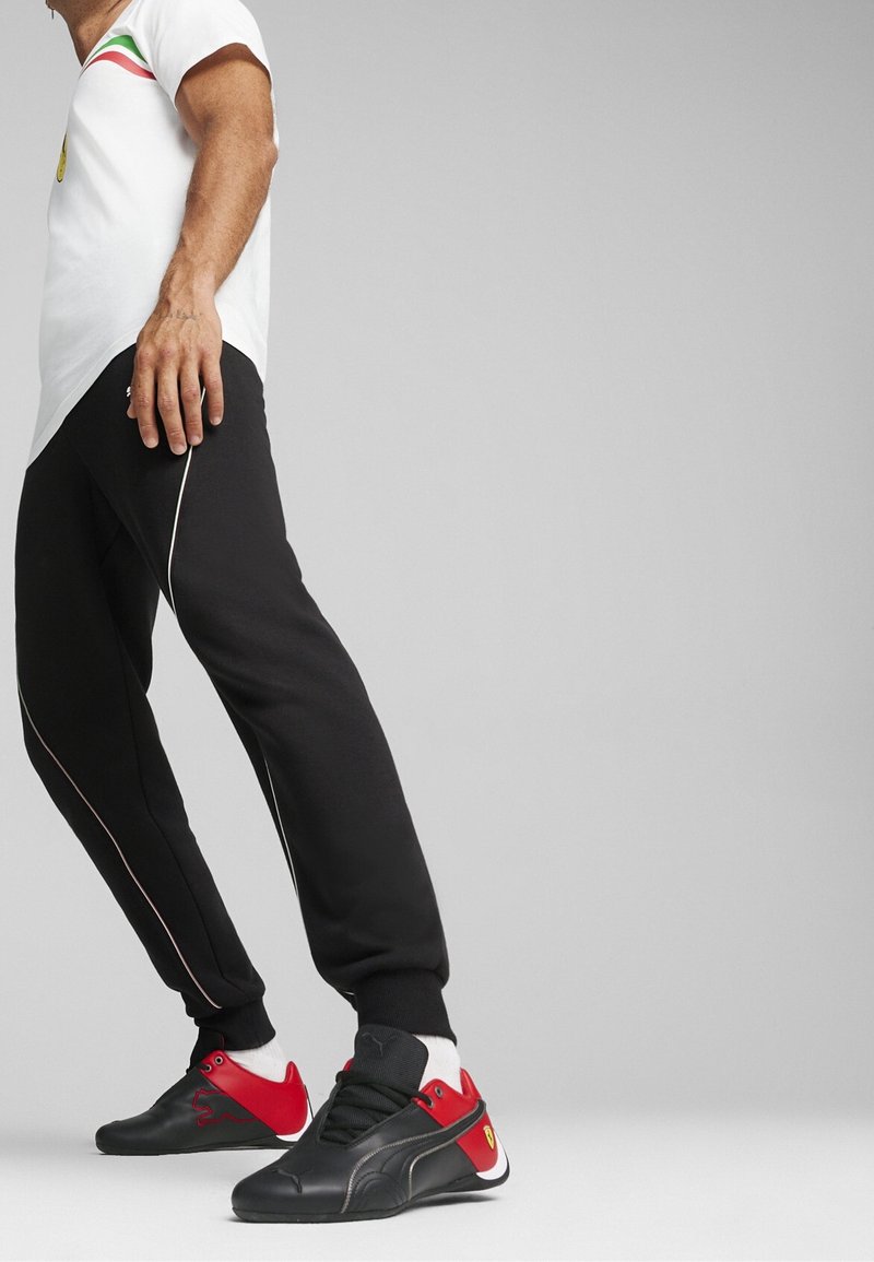 Černé tepláky s bílými lemováním, v kombinaci s černými a červenými teniskami se znakem. Hlava je bílá košile se zelenými a červenými akcenty.