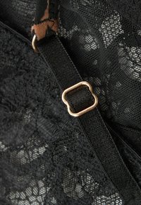 Sort blonde stof med intrikate blomster mønstre, en justerbar sort rem og et guld metalhardware-accents.