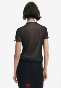 Schwarzes, transparentes Kurzarmoberteil mit einem gewellten Ausschnitt, leicht taillierter Form und glatter Textur. Trägt man über einem schwarzen, einfarbigen Rock.