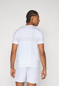 T-shirt sportivo bianco con maniche corte, scollatura rotonda e dettagli diagonali a righe in grigio e arancione sulla schiena.