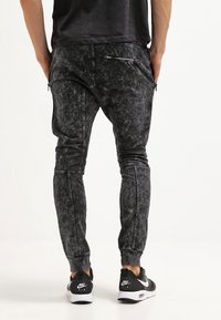 Černé joggingové kalhoty s acid-wash efekt, úzkého střihu, s kapsami na zip a elastickými manžetami, doplněné černými teniskami.