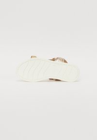 Flate sandaler med en metallisk gull overdel, justerbar stropp og en teksturert hvit gummisåle, med horisontale spor for godt grep.