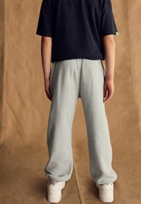 Šedé flísové tepláky s elastickými manžetami, v kombinácii s čiernym tričkom s krátkym rukávom. Jednoduchý dizajn a uvoľnená silueta. Biely sneakers.