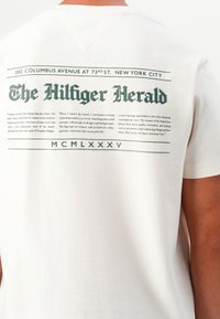T-shirt en coton blanc avec un imprimé graphique au dos présentant "The Hilfiger Herald" et du texte supplémentaire en vert foncé. Coupe ajustée.