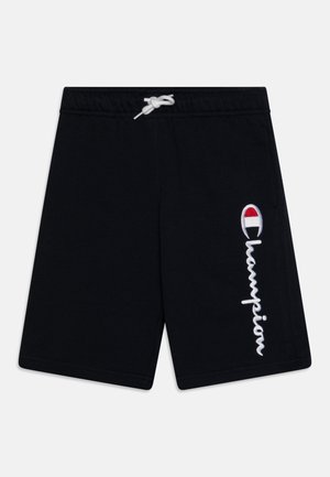 Pantalones cortos deportivos negros con cordón blanco y logo vertical blanco de "Champion" con emblema rojo y azul en la pierna derecha.