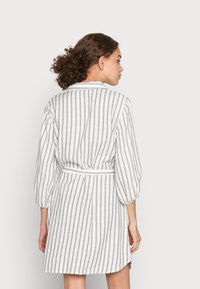 Striped, knee-length dress in light fabric; features a collar, long puffed sleeves, and a tied belt, with vertical gray and white stripes.