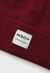 Burgunder strikket lue med tekstur, utstyrt med en rektangulær hvit etikett med "MSCH COPENHAGEN" i svart tekst.