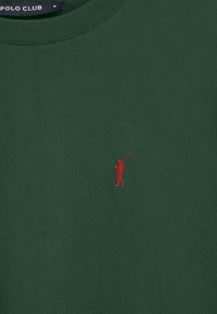 Grön bomullströja med rundad halsringning och ribbad krage, med en liten röd broderad golffigur på vänster bröst.