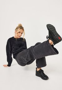 Pull noir en peluche, pantalon large gris foncé et baskets noires avec des accents texturés et un détail rouge sur la semelle.