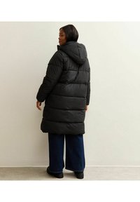 Zwarte pufferjas met een capuchon, voorzien van gestikte delen, een middenlange snit en een gladde textuur. Gecombineerd met jeans met wijde pijpen.